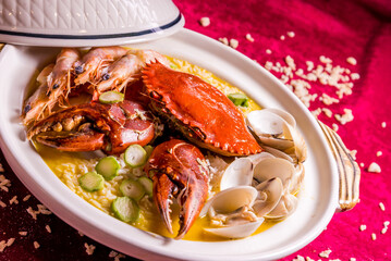 stewed mixed seafood platter crab, shell clam, tiger prawn in hot clay pot with rice and yellow chicken stock congee on red background chinese banquet menu