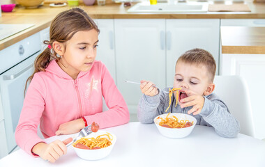 children in the kitchen at the table eat pasta.