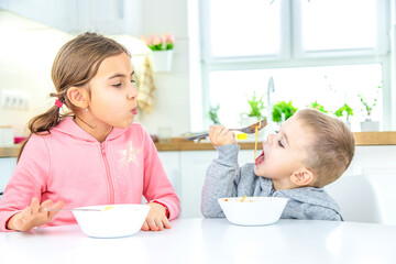 children in the kitchen at the table eat pasta.