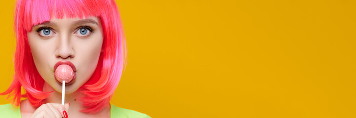 Banner format. Freaky hipster woman in pink wig eat lick lollipop on bright yellow background