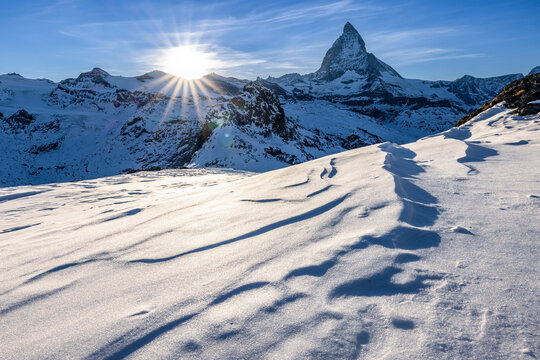 Alpine sunny winter landscape with a view of the Matterhorn, near Zermatt, in Switzerland. In the foreground an expanse of frozen snow shaped by the cold altitude wind.
