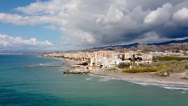 Panoramic aerial view of beautiful costal city Torrox. Drone going forward creating a beautiful  perspective of Torrox Costa. View of the lighthouse of Torrox,  river and promenade of Torrox. 
