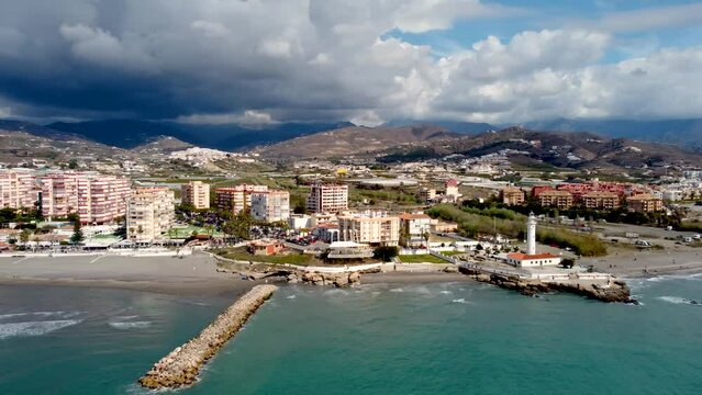 Panoramic aerial view of beautiful costal city Torrox. Drone panning right creating a beautiful circle around the lighthouse of Torrox. View of Torrox river and promenade of Torrox. Cloudy sky