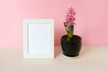 photo frame with white blank card and flowers on pastel pink background. Mock up poster frame. Stylish template.