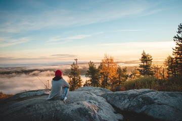 Hiker sits atop Vuokatinvaara in Sotkamo in the Kainuu region, Finland at sunrise and above the...