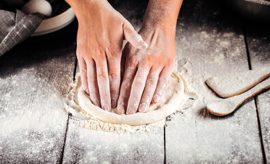 Hands kneding a dough for a pizza cooking with flour on the wooden table