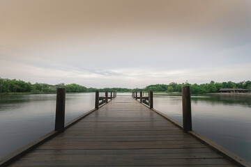 The wooden bridge stretches into the middle of the water. In the beautiful nature, evening