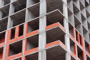 A tall residential building under construction. Orange bricks on the bottom of the frame. Concrete plates