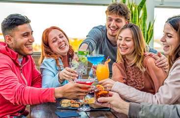young adult group of friends having cocktail on a rooftop bar restaurant outdoors. people enjoying happy hour together drinking alcohol and eating sitting on a table. fun and lifestyle concept