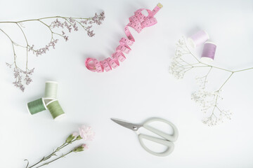 Modern arrangement  for sewing in pastel colours with sewing thread , mint green scissors, pink measuring tape and flowers on white background. Flat lay.