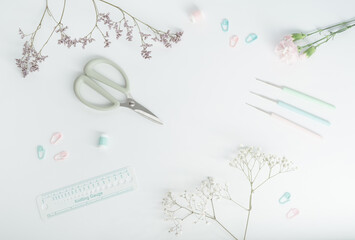 Modern, creative layout  for crocheting  in pastel colours with crochet hooks, scissors, stitch markers,  knitting gauge and flowers on white background. Flat lay.The concept of  hobby.