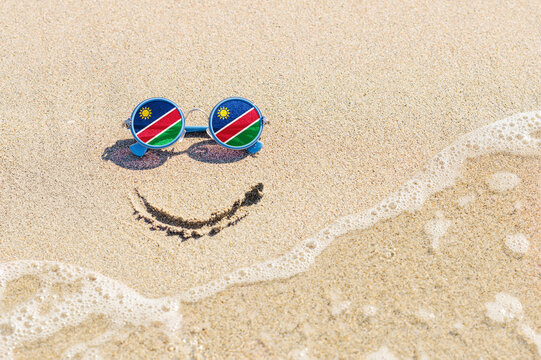A painted smile on the sand and sunglasses with the flag of the Namibia. The concept of a positive and successful holiday in the resort of the Namibia.
