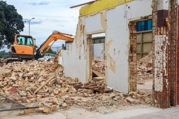 A building being demolished, with an excavator in the background