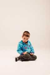 Naklejka premium Little boy sits on a white background and smiles