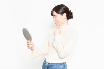 白い背景の前に立って鏡で自分の肌を見る女性