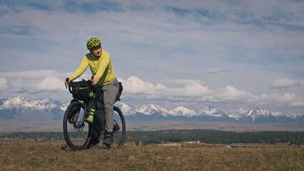 Fototapeta na wymiar The man travel on mixed terrain cycle touring with bikepacking. The traveler journey with bicycle bags. Sport tourism bikepacking, bike, sportswear in green black colors. Mountain snow capped.