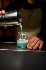 close-up of glass in which the male hand of bartender pours a blue cocktail from a shaker