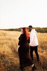Beautiful couple walking at the field, attractive husband holding hands adorable wife, overjoyed woman smiling, happy family spend time together, weekends outdoors concept