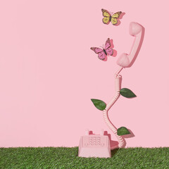 Spring creative layout with pink retro phone with butterflies and leaves on pastel pink background and green grass. 80s or 90s retro fashion aesthetic telephone and flowers concept. Surreal idea.