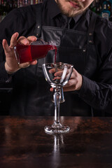 Bartender dressed in black apron and shirt make red cocktail drink on black background