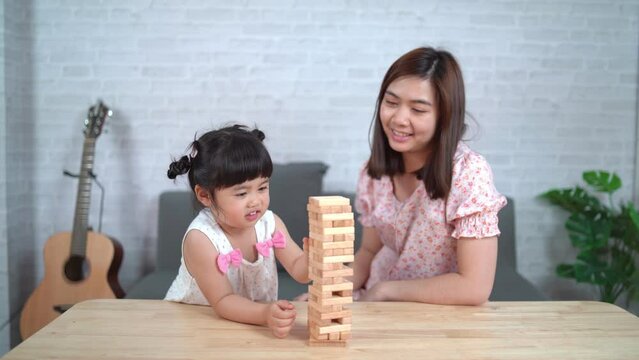 Jenga games concept. Asian daughter and mother smiling happily and laughing playing wooden jenga games sitting on sofa in living room at home, mother and daughter family activities playing happy games