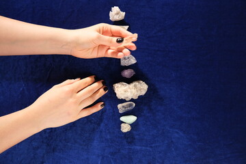 Top view female hands with black nails lying on table with gem stones. Blue velvet for background.