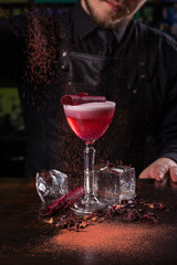 Bartender dressed in black apron and shirt make pink cocktail drink on black background