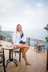 A young woman with a camera is standing in a white shirt overlooking the mediterranean sea. freelancer girl