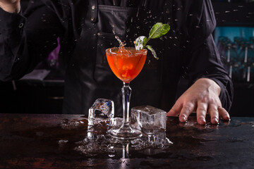 Bartender dressed in black apron and shirt make orange cocktail drink on black background