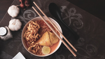Thai Food, Northern Style Curried Noodle Soup or what we call in thai "Khao Soi" served in a Thai style patterned bowl. on brown wooden table