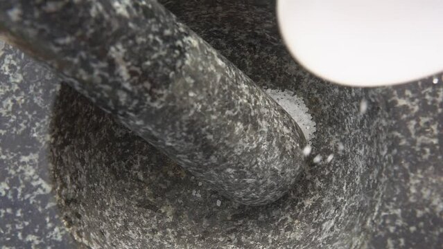 Close-up of a white sea salt falling and bouncing into the grey stone mortar 