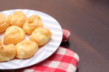 The eclair is placed in a white plate on a wooden table.