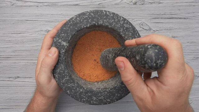 Top view of hand with pestle grinding mix of spices and peppers into the powder