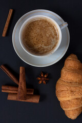 A glass of cappuccino, with fresh croissants and cinnamon sticks. 
