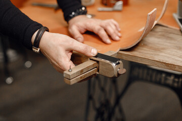 Cropped photo of a leather craftsman hands working on a belt