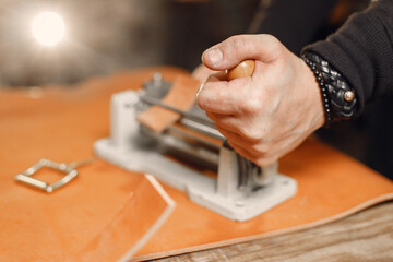 Cropped photo of a leather craftsman hands working on a belt