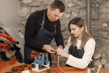 Leather craftsman with master's apprentice working on a belt