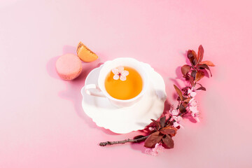 Tea with pink spring cherry blossom served in a porcelain tea cup and a macaron.
