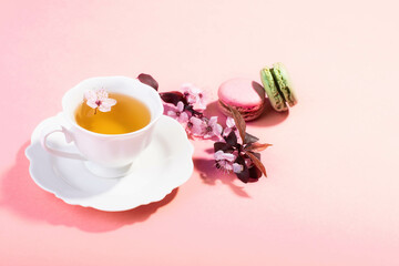 Tea with pink spring cherry blossom served in a porcelain tea cup and a macaron.