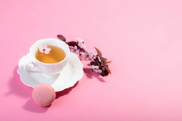 Tea with pink spring cherry blossom served in a porcelain tea cup and a macaron.