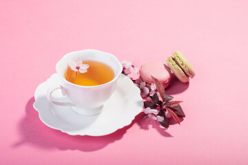 Obraz na płótnie Canvas Tea with pink spring cherry blossom served in a porcelain tea cup and a macaron.