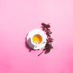 Tea with pink spring cherry blossom served in a porcelain tea cup and a macaron.