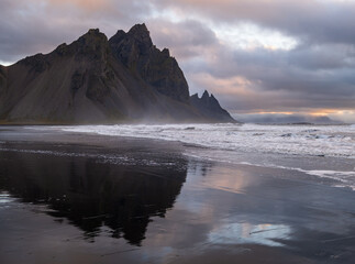Sunrise Stokksnes cape sea beach and Vestrahorn Mountain with its reflection on wet black volcanic sand surface, Iceland. Amazing nature scenery, popular travel destination.