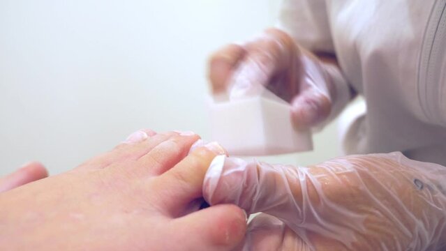 pedicurist at work files his client's toenails  using the buffer