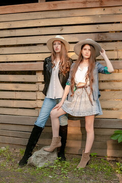 Two teen girls in rustic style clothes and wide-brimmed hats posing on wooden boards background