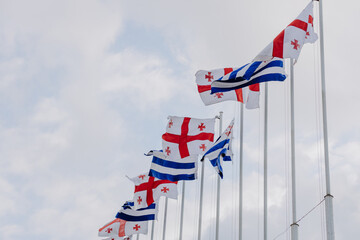  National flags of Georgia and Adjara waving in the wind against a cloudy sky. Close-up
