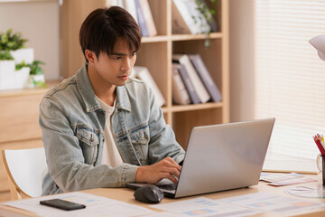 Fototapeta premium At home, a business asian man types and works online on a desk table with a laptop.