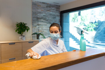 Woman in mask wiping reception desk in modern hospital