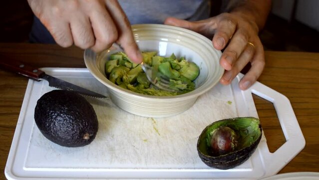 caucasian man crushing avocado in a white bowl preparing guacamole