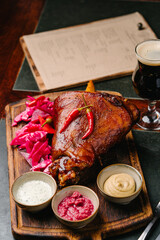 Pork knuckle stewed in beer on a wooden board with mustard, horseradish, white sauce, pickled cabbage and dark beer. Serve in the pub